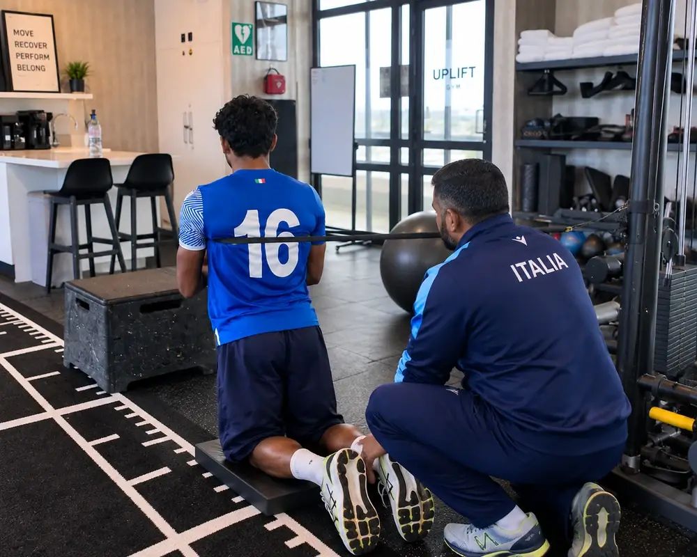 Thihan in Italy team kit coaching a player through a loaded trunk exercise in a gym